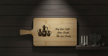 Personalized Hanukkah cutting board from The Present Spot, engraved oil lamps and family name on acacia wood, ideal Jewish gift.